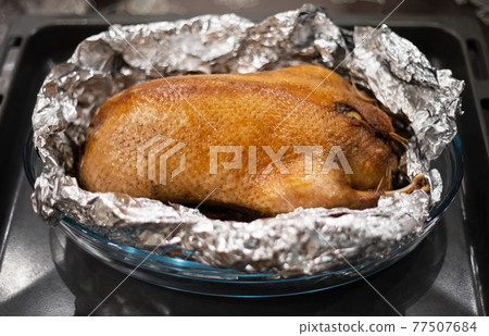 Food in foil. Duck with apples baked in foil on a tray. Delicious poultry meat with a golden crust. Food in foil. Duck with apples baked in foil on a tray. Delicious poultry meat with a golden crust. 77507684