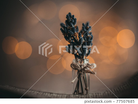 A small bouquet of lavender flowers on a brown background with Golden yellow bokeh light close up. Bunch of lavender in a tiny bottle, vase, macro. Beautiful bright bokeh. Still life with flowers. 77507685