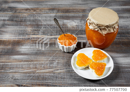 Homemade carrot jam in a glass jar and bowl on a dark brown wooden background. Homemade carrot jam in a glass jar and bowl on a dark brown wooden background. 77507700