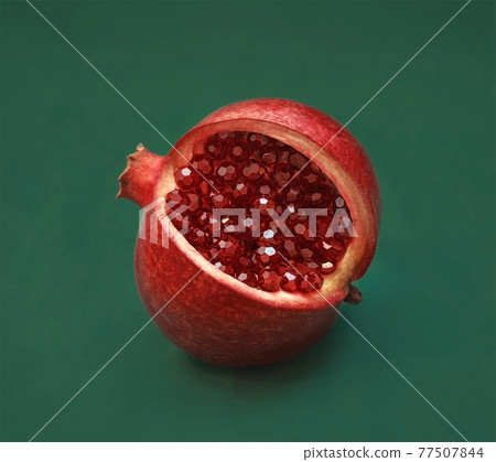 Beautiful red sliced pomegranate on a green background. Pomegranate fruit with red shiny beads, garnet crystals instead of seeds and grains. Macro, close up, abstraction. Jewelry unusual fruit. Beautiful red sliced pomegranate on a green background. Pomegranate fruit with red shiny beads, garnet crystals instead of seeds and grains. Macro, close up, abstraction. Jewelry unusual fruit. 77507844