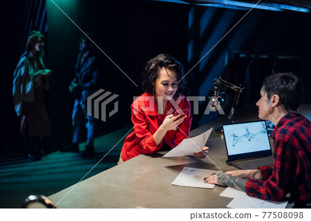 A girl talks to a young tattoo artist and chooses a tattoo based on sketches drawn on paper. Photographs a sketch on a smartphone. 77508098