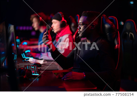 A multi-racial team of esports athletes conducts a training session before an online shooter tournament. Neon light. 77508154