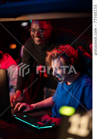 Caucasian guy shows his black friend how to play a video game in a computer club 77508155