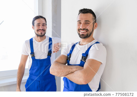 Two construction workers in overalls look at the camera Two construction workers in overalls look at the camera 77508172
