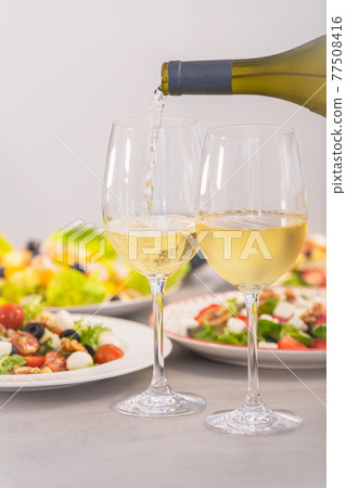 Pouring white wine next to assortment of salads: Selective focus. Healthy food and lifestyle concept. Pouring white wine next to assortment of salads: Selective focus. Healthy food and lifestyle concept. 77508416