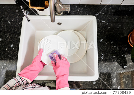 top view on female hands in gloves rinsing dishes with purple sponge above kitchen sink top view on female hands in gloves rinsing dishes with purple sponge above kitchen sink 77508429