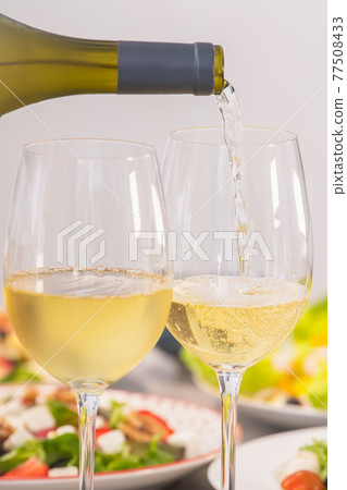 Pouring white wine next to assortment of salads: Selective focus. Healthy food and lifestyle concept. Pouring white wine next to assortment of salads: Selective focus. Healthy food and lifestyle concept. 77508433