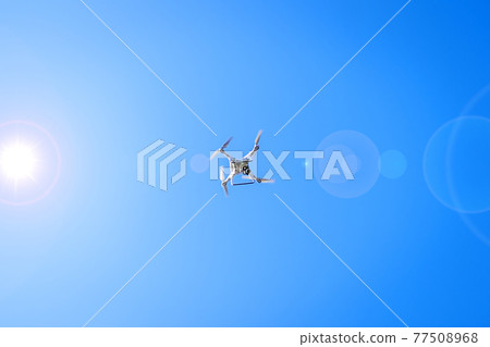 Drone flying in sunshine on blue sky background Drone flying in sunshine on blue sky background 77508968