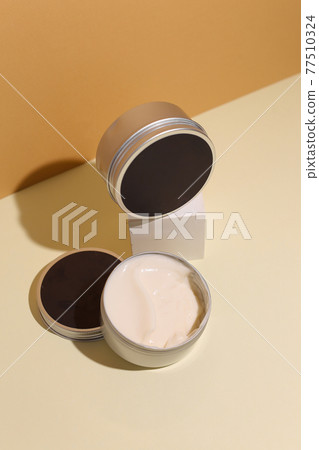 Opened container with cream on a beige background. Opened container with cream on a beige background. 77510324