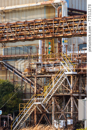 由工廠建築和在其前面運行的管道、腳手架和樓梯創建的幾何圖案 77511278