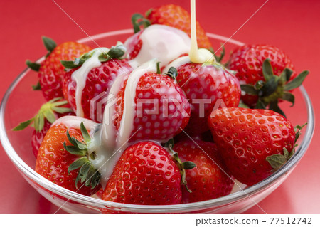 Sprinkle condensed milk on the strawberries on a glass bowl 77512742