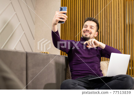 Smiling man with laptop on sofa talking on cell phone. 77513839