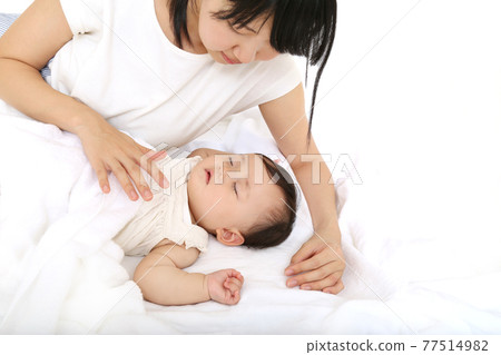 一位母親看著嬰兒在白色背景上小睡。育兒、母性、親情形象 一位母親看著嬰兒在白色背景上小睡。育兒、母性、親情形象 77514982