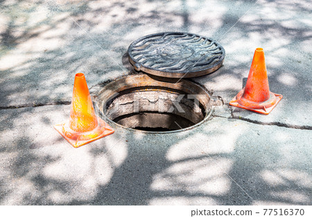 Open sewer manhole on the asphalt road 77516370