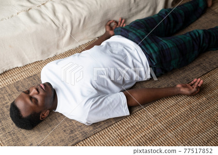 Young black man lying in Dead Body exercise or Corpse pose with his eyes closed, Savasana pose Young black man lying in Dead Body exercise or Corpse pose with his eyes closed, Savasana pose 77517852