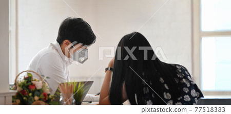 Photo of young couple that wearing a medical mask sitting and relaxing together at the wooden working desk over comfortable living room as background. Photo of young couple that wearing a medical mask sitting and relaxing together at the wooden working desk over comfortable living room as background. 77518383