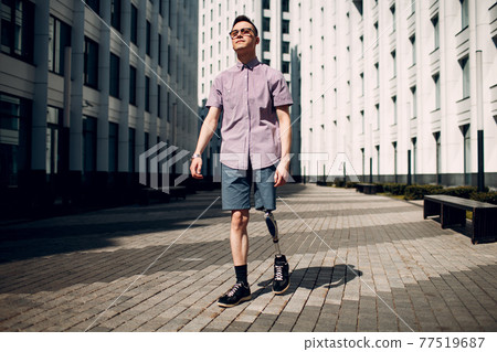 Disabled young man with leg prosthesis walking street 77519687