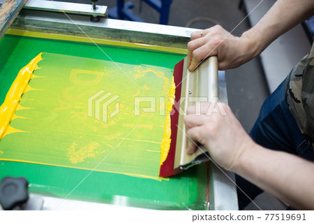 Serigraphy silk screen print process at clothes factory. Frame, squeegee and plastisol color paints Serigraphy silk screen print process at clothes factory. Frame, squeegee and plastisol color paints 77519691