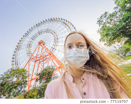 A woman in a pink dress takes a selfie on the background of a ferris wheel 77519707