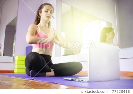 Fitness and yoga trainer teaches via laptop. Wireless technology in sports, self-isolation . The girl shows exercises in the gym on the mat. The concept of distance learning. 77520418