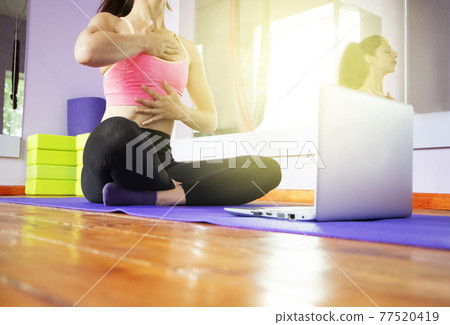 Fitness and yoga trainer teaches via laptop. Wireless technology in sports, self-isolation . The girl shows exercises in the gym on the mat. The concept of distance learning. 77520419