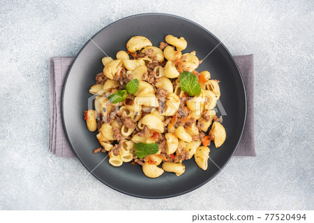 Stewed pasta with minced beef and vegetables, macaroni in Navy style on a plate. grey concrete background. Copy space. 77520494