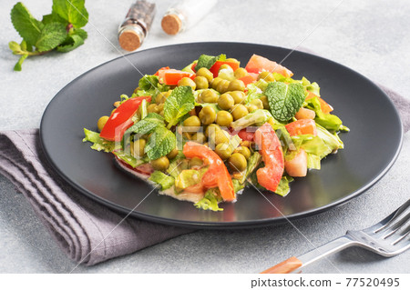 Salad of green tomato leaves and canned peas seasoned with sauce on a black plate. Spring fresh diet salad. top view Salad of green tomato leaves and canned peas seasoned with sauce on a black plate. Spring fresh diet salad. top view 77520495