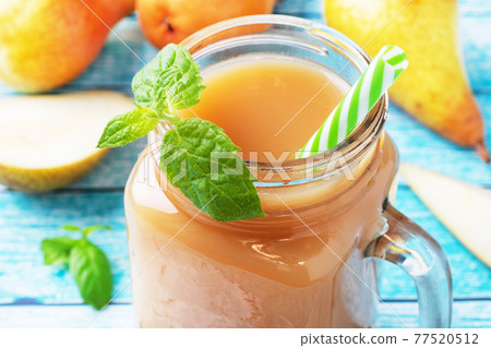 Natural pear juice in a glass cup. Juicy ripe conferences pears and mint leaves. Bright blue background. 77520512