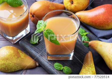 Natural pear juice in a glass cup. Juicy ripe conferences pears and mint leaves. Dark rustic wooden background. 77520514