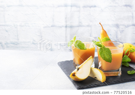 Natural pear juice in a glass cup. Juicy ripe conferences pears and mint leaves. copy space Slate stand, light concrete background. 77520516