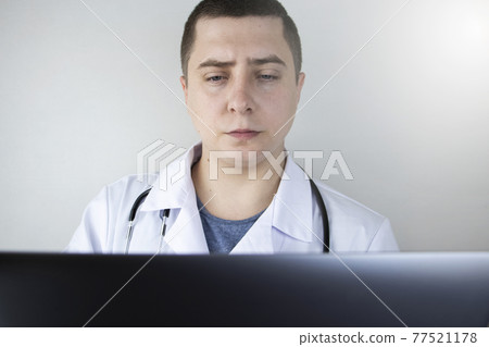 Workplace of a doctor. Male therapist works at a computer. The concept of modern medicine and technology used by medical professionals Workplace of a doctor. Male therapist works at a computer. The concept of modern medicine and technology used by medical professionals 77521178