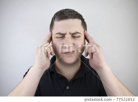 A man holds his head with his hands. Sensation of headache, migraine and dizziness. Headaches from stress or overwork 77522852