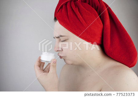 Funny man with a red towel on his head sniffs, tastes and smears a cream on his face. The concept of male self-care, spa treatments and male cosmetics Funny man with a red towel on his head sniffs, tastes and smears a cream on his face. The concept of male self-care, spa treatments and male cosmetics 77523373