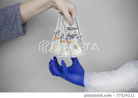 Patient's hand holds out money to the doctor. The concept of corruption in healthcare, bribery or paid medicine 77524111