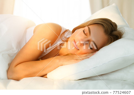 Beautiful blonde girl sleeping sweetly in sunny bedroom on a white bed. Holyday comfort and Rest concepts 77524607