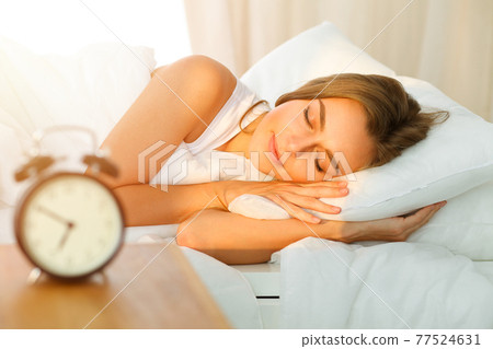 Beautiful blonde girl sleeping sweetly in sunny bedroom on a white bed. Holyday comfort and Rest concepts 77524631