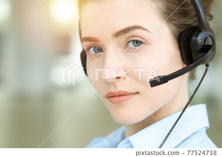 Beautiful female specialist with headphones helping customers online and smiling charmingly in sunny call center office. Business people concept Beautiful female specialist with headphones helping customers online and smiling charmingly in sunny call center office. Business people concept 77524738