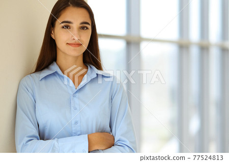 A friendly young dark hair businesswoman or female student is standing with some papers in the office A friendly young dark hair businesswoman or female student is standing with some papers in the office 77524813