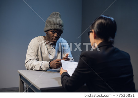 A black guy listens to his rights from a civil lawyer at a table in a visiting room in a state prison A black guy listens to his rights from a civil lawyer at a table in a visiting room in a state prison 77526851