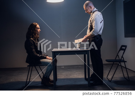 A white male police detective talks to a suspect in a drug trafficking case who is sitting in an interrogation room in handcuffs. A white male police detective talks to a suspect in a drug trafficking case who is sitting in an interrogation room in handcuffs. 77526856