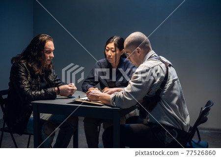 In the police station's interrogation room, good and bad cops are questioning a theft suspect in a leather jacket. In the police station's interrogation room, good and bad cops are questioning a theft suspect in a leather jacket. 77526860