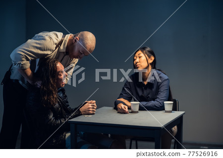 A suspect in a police station laughs madly during an interrogation conducted by investigators 77526916
