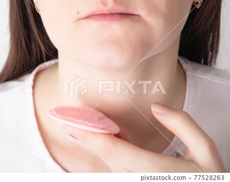 The girl holds a silicone brush for cleaning the face with gel mousse to clean the pores of the skin on the chin, Dermatology The girl holds a silicone brush for cleaning the face with gel mousse to clean the pores of the skin on the chin, Dermatology 77528263