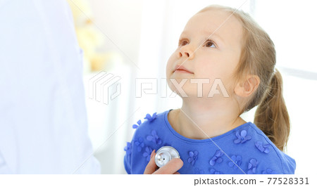 Doctor examining a little girl by stethoscope. Happy smiling child patient at usual medical inspection. Medicine and healthcare concepts 77528331