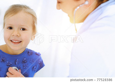 Doctor examining a little girl by stethoscope. Happy smiling child patient at usual medical inspection. Medicine and healthcare concepts Doctor examining a little girl by stethoscope. Happy smiling child patient at usual medical inspection. Medicine and healthcare concepts 77528386