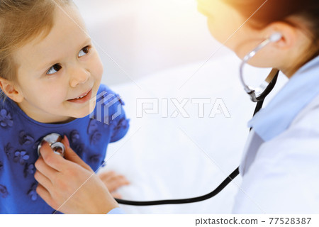 Doctor examining a little girl by stethoscope. Happy smiling child patient at usual medical inspection. Medicine and healthcare concepts Doctor examining a little girl by stethoscope. Happy smiling child patient at usual medical inspection. Medicine and healthcare concepts 77528387