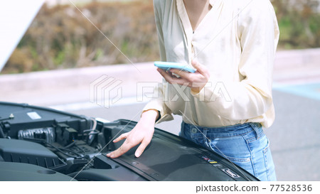 一位女士拿著智能手機打開汽車故障道路服務的引擎蓋 77528536