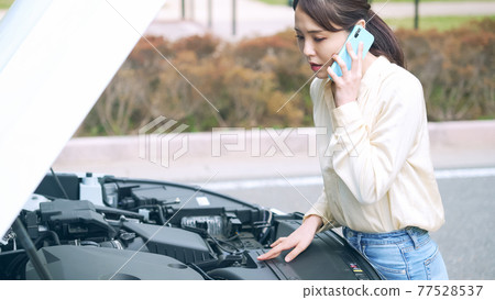 A woman who opens the hood of a car and talks on a smartphone. Road service 77528537