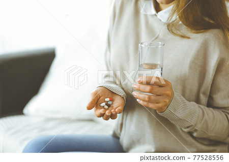 Close-up woman holding pills time to take medications, cure for headache, high blood pressure pain killer drugs at home. Stay at home concept during Coronavirus pandemic 77528556