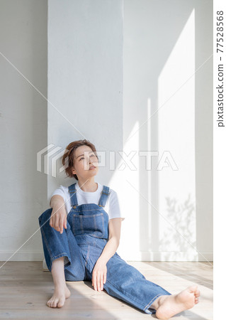 Genderless LGBT boy-like girl wearing overalls and sitting on the floor Genderless LGBT boy-like girl wearing overalls and sitting on the floor 77528568